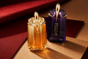 Mugler Alien Goddess gold perfume bottle and Alien purple perfume bottle styled on luxurious red and gold textures.