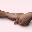 Two hands applying Aesop Eleos Aromatique Hand Balm on each other on a light pink background