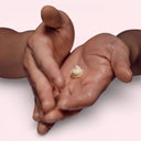 Two hands holding a small amount of Aesop Eleos Aromatique Hand Balm cream against a light pink background