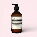 Brown Aesop Geranium Leaf Body Balm 500ml bottle on a pink background