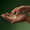 Two hands with a small amount of Aesop Geranium Leaf Body Balm cream  on a dark green background