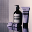 Aesop Eleos Aromatique product range on a reflective surface with a tiled wall background