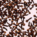 Close-up of a pile of clove buds on a light pink background