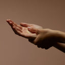 Hands applying Aesop Resurrection Aromatique Hand Balm against a brown background