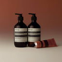Aesop Rind Concentrate Body Balm including bottles and a tube on a beige background