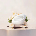 Ariana Grande Mod Vanilla Eau De Parfum 30ml fragrance moood image: White oval shaped perfume bottle with 'Ariana Grande' logo surrounded with white orchids and vanilla beans  on a light background | BEAUTE KNOWS AUSTRALIA