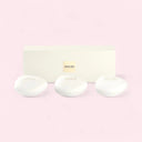 Three white oval soap bars including Thé Yulong, Pivoine Suzhou, and Vétiver d’Hiver from the Armani Privé Les Eaux Hand Soaps Discovery Trio Gift Set in front of its rectagular white packaging box a light pink background | BEAUTE KNOWS AUSTRALIA