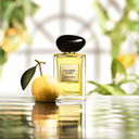 Armani Privé Orangerie Venise Eau de Toilette 100ml perfume bottle next to a lemon on a reflective surface with blurred greenery in the background.