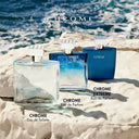 Three Azzaro Chrome perfume bottles on a rocky surface with ocean in the background