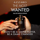 Azzaro The Most Wanted Eau de Parfum Intense 50ml perfume bottle being held with promotional text on a dark background
