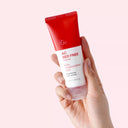 BEAUTE KNOWS Hand holding a tube ofBeauty of Majesty BOM AC Red Free Cream 50ml with a red and white design.