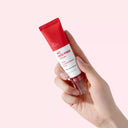 BEAUTE KNOWS Hand holding a red and white Beauty of Majesty BOM AC Red Free Serum 30ml tube against a light pink background