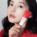BEAUTE KNOWS Woman holding a red Beauty of Majesty BOM AC Red Free Serum 30ml tube against a gray background