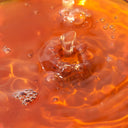 Close-up of Beauty of Majesty BOM Just One Houttuynia Cordata Extract Toner droplet impacting orange liquid with visible bubbles.