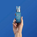 Hand holding a blue skincare bottle against a blue background
