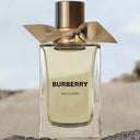 Burberry Ash Flower perfume bottle with a gold cap and bow on a blurred natural background