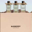 Three Burberry perfume bottles with a beige box in the foreground on a blurred natural background