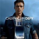 Calvin Klein Defy perfume bottle with Richard Madden in a denim jacket against a blue sky.