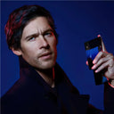 Man holding a blue and black coloured Carolina Bad Boy Colbalt Elixir Perfume bottle with a blue gradient background