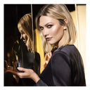 Model Karlie Kloss holding a Carolina Herrera Good Girl Supreme Eau De Parfum bottle in front of a mirror, gold coloured background