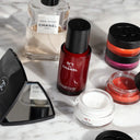 Chanel beauty products including a Chanel N°1 De Chanel Revitalizing Serum & Cream Duo Set, a perfume bottle, lip products, and compact mirror on a marble surface.