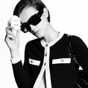 A model wearing Chanel sunglasses and signature black and white  holding a La Crème Main hand cream 50ml bottle