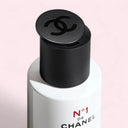 Close-up of a Chanel No. 1 Red Camelia Powder to Foam Cleanser bottle with open cap on a pink background