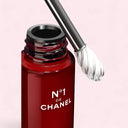 Red Chanel N°1 De Chanel Revitalizing Eye Serum 15ml bottle with an applicator on a pink background