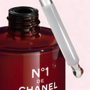 Red Chanel N°1 De Chanel Revitalizing Serum 50ml bottle with dropper on a pink background