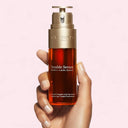 Hand holding a bottle of Clarins Double Serum 50ml bottle against a pink background