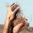 Hand wearing silver rings holding roots, against a blurred natural background