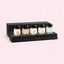 Set of five Armani Priveperfume bottles with black lids on a decorative black stand against a light pink background