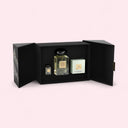 Perfume set with a bottle and two boxes in an open black box on a light pink background