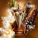 Jean Paul Gaultier Gaultier Divine Elixir Parfum 100ml perfume bottle with gold cap and brown body, surrounded by flowers and leaves on a warm-toned background.