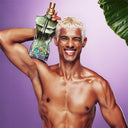 BEAUTE KNOWS Man holding a green Jean Paul Gaultier Le Beau Paradise Garden Eau De Parfum 125ml perfume bottle against a purple background