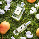 BEAUTE KNOWS Two Jo Malone London English Pear & Sweet Pea Cologne bottles on grass with apples and flowers