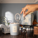 Hand holding a micro teapot in a cozy room with Jo Malone London Lavender & Moonflower Scented Candle - Limited Edition Little Greene Collection and decorative elements.