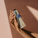 Hand holding a tube of L'occitane 20% Shea Butter Hand Cream against a warm-toned background