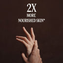 Hand with a focus on skin texture against a dark background with text '2X More Nourished Skin'.