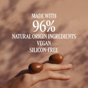 Hand holding two brown nuts with text about natural ingredients and vegan status on a brown background