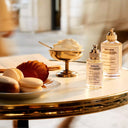 Two bottles of Maison Margiela Replica Afternoon Delight Eau de Toilette perfume on a table with pastries and ice cream.