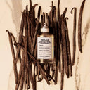 Maison Margiela Replica Afternoon Delight Eau de Toilette 100ml perfume bottle surrounded by vanilla beans on a marble surface