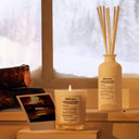 Maison Margiela Replica By the Fireplace Scented Diffuser and candle with polaroid picture and wood with background of snow