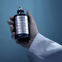 BEAUTE KNOWS Hand holding a Maison Margiela Replica Celestial Whisper fragrance bottle with a blue background