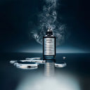 BEAUTE KNOWS Bottle of Maison Margiela Replica Celestial Whisper perfume with silver liquid drops and smoke on a dark background