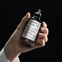 Hand holding a Maison Margiela Replica Fantasies Dancing On The Moon Eau de Parfum 100ml bottle with a black background