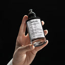 Hand holding a Maison Margiela Replica Fantasies Flying Eau de Parfum 100ml perfume bottle against a black background