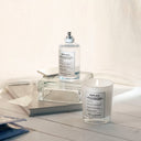 Maison Margiela Replica Lazy Sun Morning Eau de Toilette 100ml perfume bottle and candle on a wooden surface with a white background