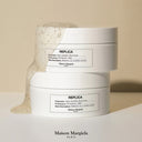 BEAUTE KNOWS Two white Maison Margiela Replica Lazy Sunday Morning Body Scrub 200ml containers on a beige background