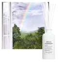 White Maison Margiela Replica When the Rain Stops Scented Diffuser 185ml diffuser bottle against a scenic background with rainbow and trees